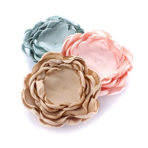 May include: Three fabric flowers in different colors: light blue, light pink, and beige. The flowers are made of multiple layers of fabric and have a ruffled appearance.