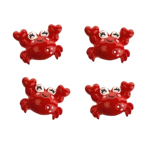 May include: Four red plastic crab figurines with white eyes and a smiling mouth. The crabs have a cartoon-like appearance.