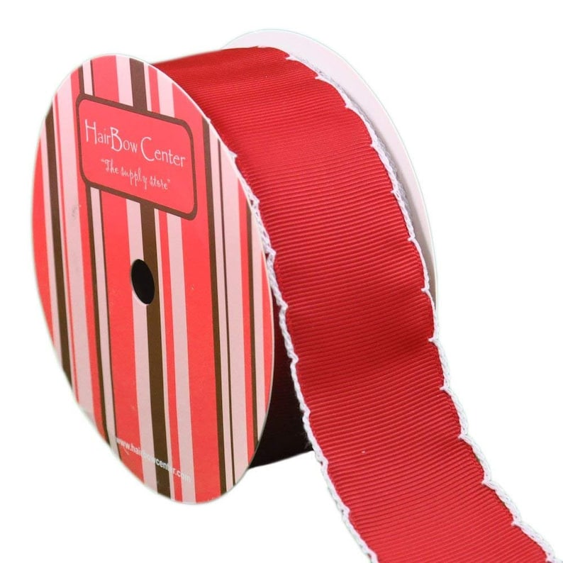 Op de afbeelding: Een rol rood lint met witte gegolfde randen. Het lint zit op een rol met een label waarop "Hair Bow Center" en "The supply store" staat.