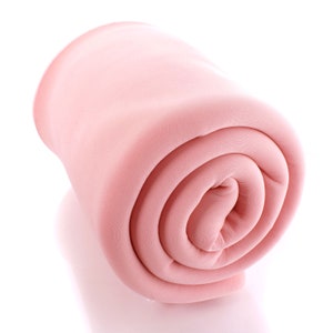 Op de afbeelding: Een opgerolde roze fleece deken. De deken is zacht en pluche, perfect om te knuffelen op de bank.