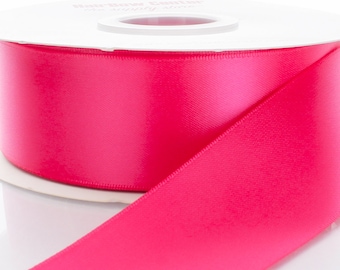 Puede incluir: Una bobina de cinta de satén rosa brillante. La cinta está enrollada alrededor de una bobina blanca con una etiqueta que dice "Hair Bow Glitter".