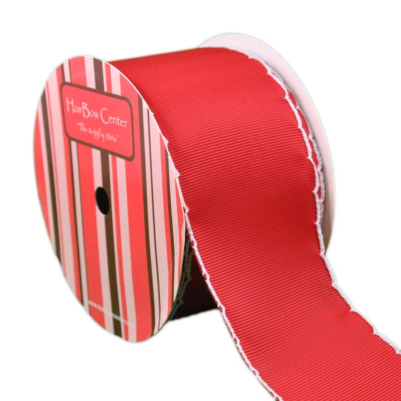 Op de afbeelding: Een rol rood lint met witte gegolfde randen. De rol is gelabeld met "HairBow Center" met de tagline "The supply store".