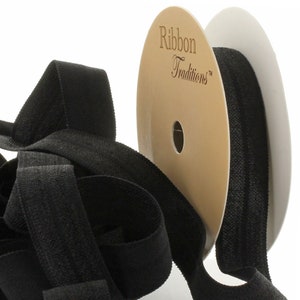 May include: Black ribbon on a spool with the text "Ribbon Traditions". The ribbon is a solid black color and appears to be made of a soft, textured material. The spool is tan and white.
