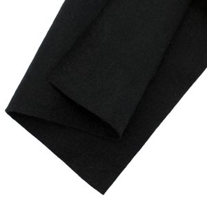 May include: A close-up shot of black felt fabric, folded and layered. The material appears soft and has a slightly textured surface. The felt is a solid, deep black color, with no visible patterns or designs.