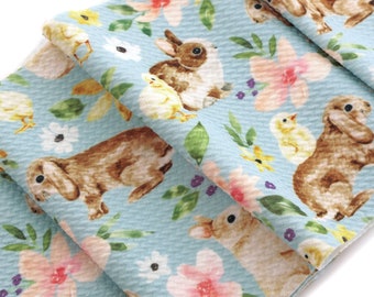 May include: A blue fabric with a repeating pattern of brown bunnies, yellow chicks, and pink and white flowers. The fabric has a textured waffle weave.