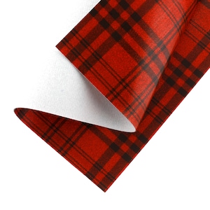 Op de afbeelding: Close-up van een rood en zwart geruit patroon stof. De stof is dubbelgevouwen, waardoor een witte achterkant zichtbaar wordt. Het ruitpatroon heeft een klassiek tartanpatroon, met elkaar kruisende lijnen die een rasterachtig uiterlijk creëren. De stof heeft een getextureerd oppervlak.