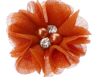 May include: An orange fabric flower with layered petals and a mesh-like texture. The center features two faux pearl beads and two clear, faceted rhinestones. The flower is set against a white background.