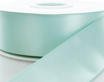 Puede incluir: Un carrete de cinta de satén azul claro. La cinta está enrollada alrededor de un carrete blanco.