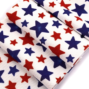 May include: White fabric with a repeating pattern of red and blue stars. The stars vary in size and are scattered across the fabric. The fabric is folded, showing the pattern from different angles.