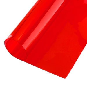 Könnte beinhalten: Ein leuchtend rotes Blatt aus transparentem Kunststoff, aufgerollt und teilweise abgewickelt, das seine glatte, glänzende Oberfläche zeigt.