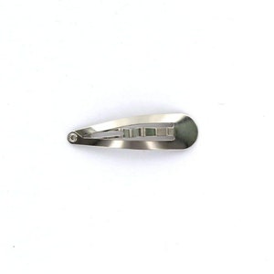 May include: A silver metal hair clip with a smooth, oval shape. The clip has a single row of teeth for holding hair in place.
