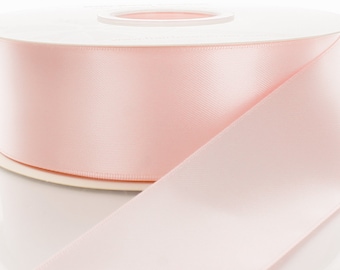May include: A spool of pale pink satin ribbon. The ribbon is wound around a white cardboard spool with a hole in the center.