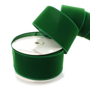 May include: A spool of emerald green velvet ribbon with a wired edge. The ribbon is 2.5 inches wide and is wrapped around a white cardboard spool with the text "www.hairbowcenter.com".