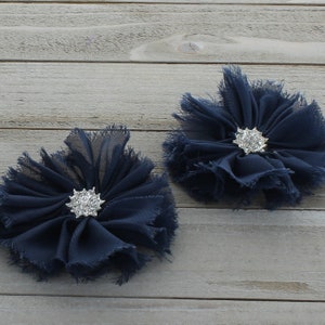 May include: Two navy blue chiffon flowers with a rhinestone centre. The flowers are on a light wood background.