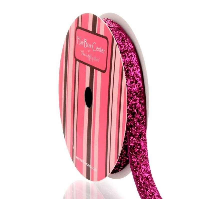 May include: A spool of pink glitter ribbon with a white label that says "Hair Bow Center, The supply store".