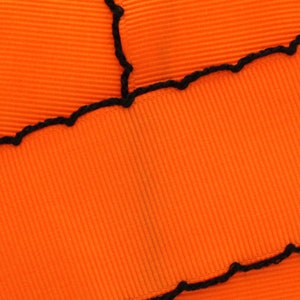 Puede incluir: Tela naranja con una puntada en zigzag negra a lo largo del borde.