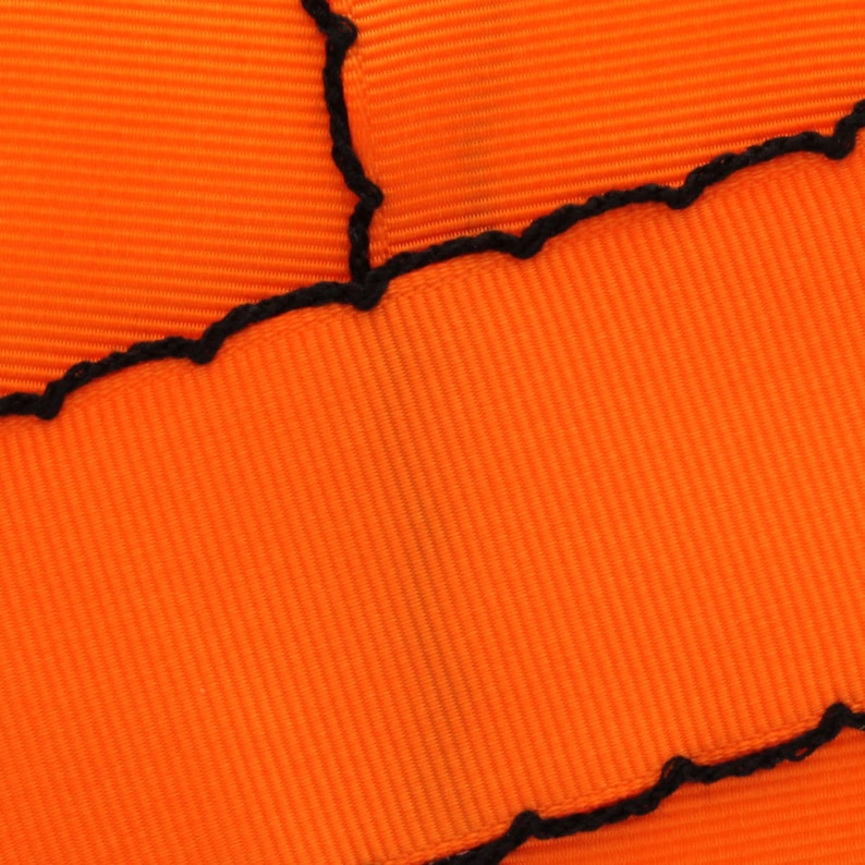 Puede incluir: Tela naranja con una puntada en zigzag negra a lo largo del borde.