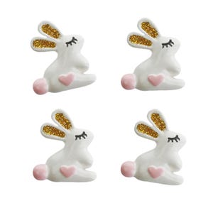 以下が含まれることがあります： 金色のグリッターの耳とピンクのハートが付いた白いセラミックのウサギの置物4つ。各ウサギは目を閉じ、黒いまつげをしています。