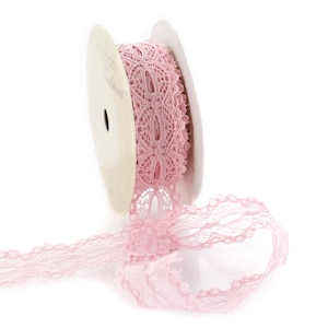 May include: A spool of pink lace ribbon with the text "Ribbon Traditions" on the spool. The lace is delicate and has a floral pattern.