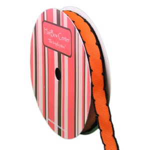 Puede incluir: Una bobina de cinta naranja y negra con un borde festoneado. La cinta est&aacute; en una bobina con una etiqueta a rayas rosa y marr&oacute;n que dice "HairBow Center, The supply store".