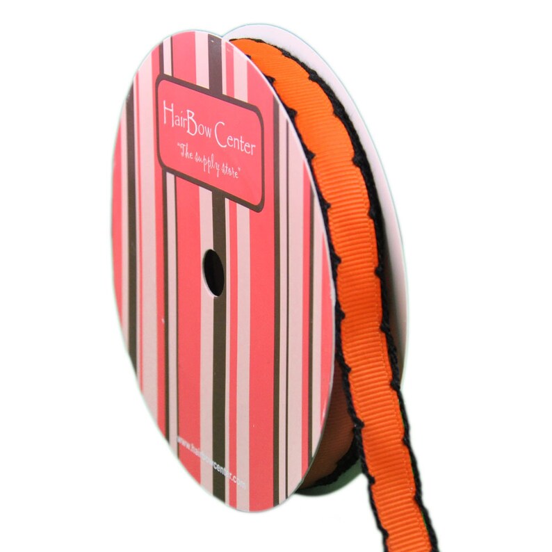 Puede incluir: Una bobina de cinta naranja y negra con un borde festoneado. La cinta est&aacute; en una bobina con una etiqueta a rayas rosa y marr&oacute;n que dice "HairBow Center, The supply store".
