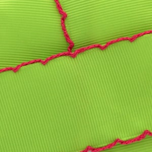 May include: Green fabric with a pink zig-zag stitch along the edges. The fabric has a ribbed texture.