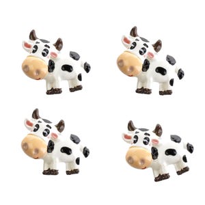 May include: Four white and black cow figurines with brown hooves and black eyes. The cows are facing the right side of the image.