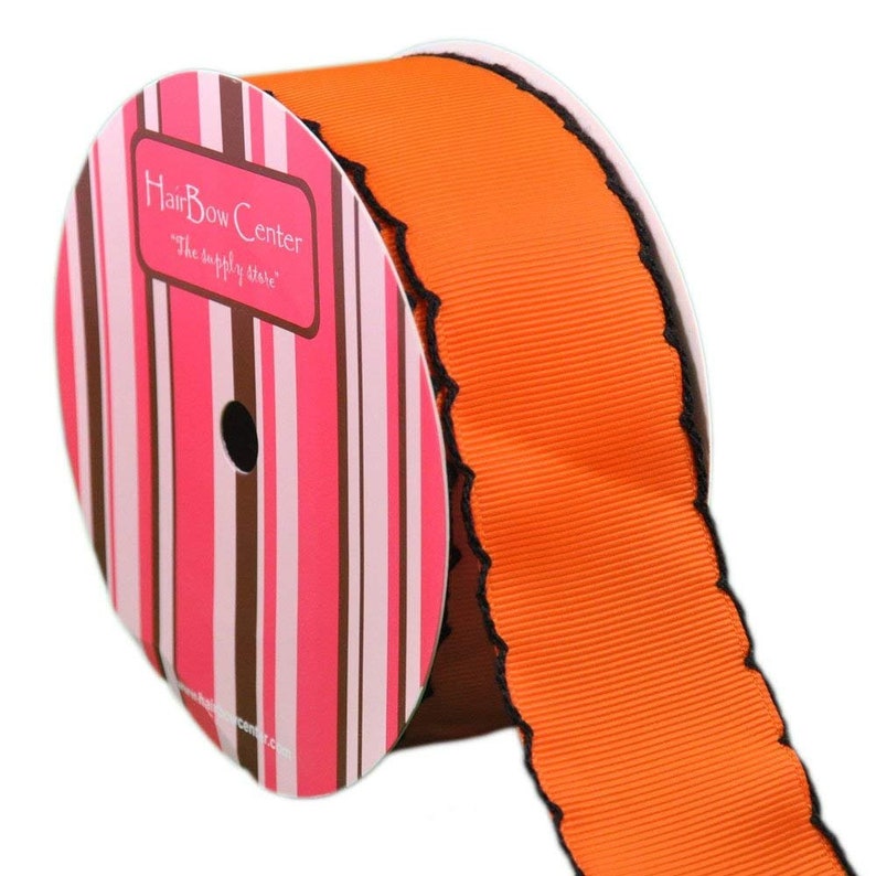 Puede incluir: Cinta naranja y negra festoneada con borde negro. La cinta est&aacute; enrollada alrededor de un carrete con una etiqueta a rayas rosa y marr&oacute;n que dice "HairBow Center" y "The supply store".