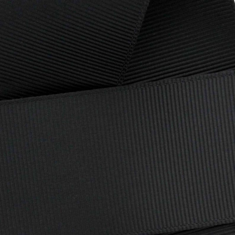 May include: Black grosgrain ribbon with a textured, ribbed surface. The ribbon is folded in half, showing the underside of the fabric.