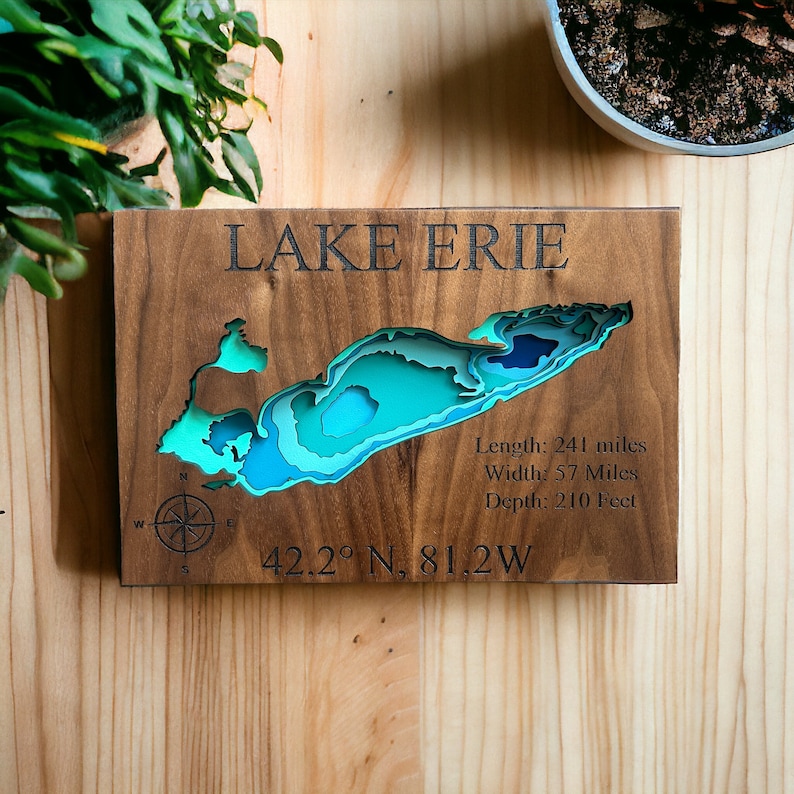 Puede incluir: Un mapa de madera del lago Erie con un dise&ntilde;o en capas azul y verde. El mapa incluye las dimensiones del lago: Longitud: 241 millas, Ancho: 57 millas, Profundidad: 210 pies. Las coordenadas 42.2&deg; N, 81.2W tambi&eacute;n est&aacute;n incluidas.
