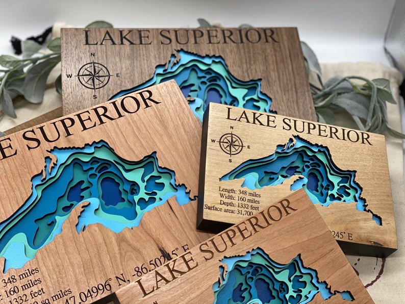 Puede incluir: Tres placas de madera con un mapa en relieve del Lago Superior. Las placas est&aacute;n hechas de diferentes tipos de madera y tienen una rosa de los vientos y texto con las dimensiones del lago. El texto dice: "Lago Superior", "Longitud: 348 millas, Ancho: 160 millas, Profundidad: 1332 pies, &Aacute;rea de superficie: 31,700" y "17.04996&deg; N, -86.50245&deg; E".