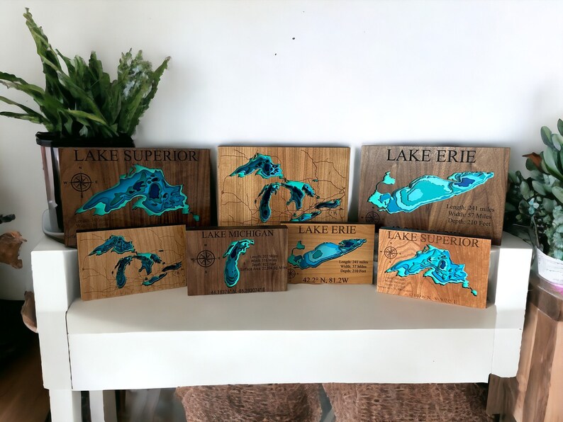 Puede incluir: Seis placas de madera con mapas de los Grandes Lagos cortados con l&aacute;ser. Cada placa presenta un lago diferente: Superior, Michigan, Erie y Ontario. Las placas est&aacute;n te&ntilde;idas de un color marr&oacute;n claro y tienen un mapa azul verdoso del lago con curvas de nivel. Las placas est&aacute;n dispuestas en fila en un estante blanco.