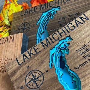Puede incluir: Un letrero de madera con un mapa en relieve azul y verde del lago Michigan. El letrero incluye el texto "LAKE MICHIGAN" y las dimensiones del lago: Longitud: 307 millas, Ancho: 118 millas, Profundidad: 922 pies, &Aacute;rea de superficie: 22.394 millas cuadradas.