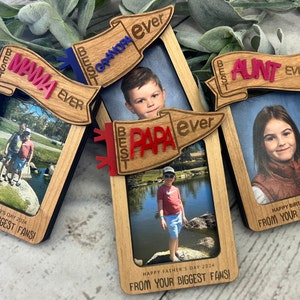 Puede incluir: Tres marcos de fotos de madera con una pancarta unida a la parte superior de cada marco. Las pancartas están decoradas con las palabras "Best", "Mama", "Ever", "Best", "Grandpa", "Ever", "Best", "Aunt", "Ever", "Best", "Papa", "Ever". Los marcos contienen fotos de personas y el texto "Happy Mother's Day 2024", "From Your Biggest Fans!" y "Happy Father's Day 2024", "From Your Biggest Fans!" y "Happy Birthday 2024", "From Your Biggest Fans!"