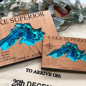Puede incluir: Dos placas de madera con un mapa 3D del Lago Superior. Las placas est&aacute;n hechas de madera de cerezo y cuentan con una rosa de los vientos, las coordenadas del lago y sus dimensiones en millas y pies. El texto "LAKE SUPERIOR" est&aacute; grabado en ambas placas.