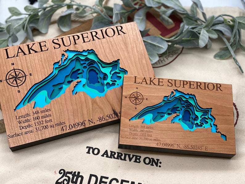 Puede incluir: Dos placas de madera con un mapa 3D del Lago Superior. Las placas est&aacute;n hechas de madera de cerezo y cuentan con una rosa de los vientos, las coordenadas del lago y sus dimensiones en millas y pies. El texto "LAKE SUPERIOR" est&aacute; grabado en ambas placas.