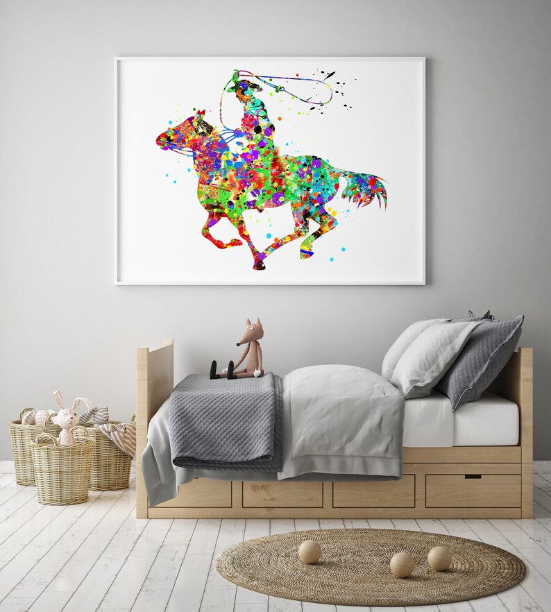 May include: A framed watercolour print depicting a cowboy on horseback, created in a vibrant splatter-paint style. The artwork shows a cowboy with a lasso, riding a horse with colourful splashes of red, blue, green, and yellow. The print is displayed above a child's bed.