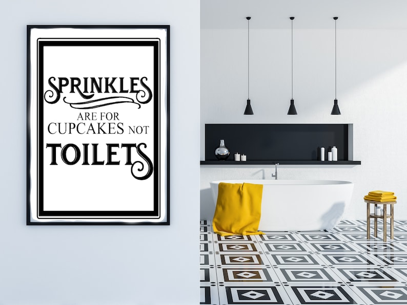 May include: Black and white framed bathroom sign with the text "Sprinkles are for cupcakes not toilets". The sign is hanging on a white wall in a bathroom with a white bathtub, yellow towel, and black and white tiled floor.
