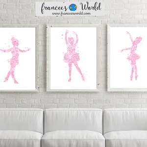 May include: Three framed watercolor prints of pink ballerina silhouettes on a white brick wall. The ballerinas are in different poses, with their arms outstretched and their legs in various positions. The prints are all the same size and are arranged in a row.