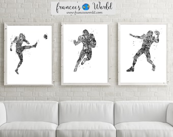 May include: Three black and white watercolour paintings of football players in action. The players are silhouetted against a white background. The paintings are framed and hung on a white brick wall.