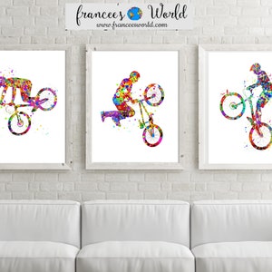 May include: Three framed watercolor paintings of a person performing a stunt on a bicycle. The paintings are in a variety of colors, including red, blue, green, yellow, and purple. The paintings are hung on a white brick wall above a white couch.