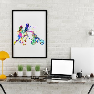 May include: A framed watercolor painting of a family with a child in a stroller. The painting is in a black frame and is hanging on a white brick wall. There is a laptop, a lamp, and plants on a wooden table in front of the painting.