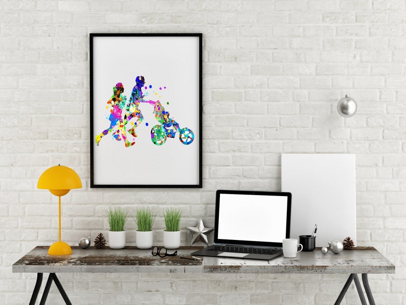 May include: A framed watercolor painting of a family with a child in a stroller. The painting is in a black frame and is hanging on a white brick wall. There is a laptop, a lamp, and plants on a wooden table in front of the painting.