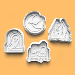Może przedstawiać: Cztery białe wykrawacze do ciastek o tematyce Halloween. Projekty obejmują ducha w nagrobku, nietoperza przed półksiężycem, nawiedzony dom i scenę cmentarza z krzyżem.