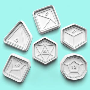 May include: Set of six white plastic cookie cutters shaped like dice with numbers 4, 6, 8, 10, 12, and 20.