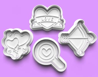 May include: Set of four white plastic cookie cutters shaped like a heart with a banner that says "LOVE", a heart inside a magnifying glass, a heart with balloons, and an arrow and bow.