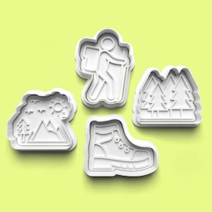 May include: Four white plastic cookie cutters in the shapes of outdoor adventure icons. The shapes include a hiker with a backpack, a hiking boot, a mountain scene with trees and sun, and a pair of trees.