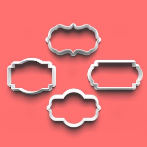 May include: Four white plastic cookie cutters shaped like different frames. The frames are all different sizes and have different decorative edges.