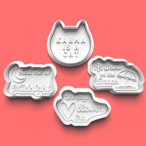 May include: Set of four white cookie cutters with various phrases and designs. The cutters feature the phrases "Karma is a Cat", "Meet me at Midnight", "In my Lover Era", and "Snow on the Beach".