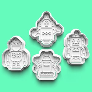 以下が含まれることがあります： 4つの白いプラスチック製のロボット型クッキーカッター。各カッターは、アンテナ、腕、顔の特徴などの詳細を備えた、異なるロボットデザインを特徴としています。カッターは、無地のティール色の背景に配置されています。
